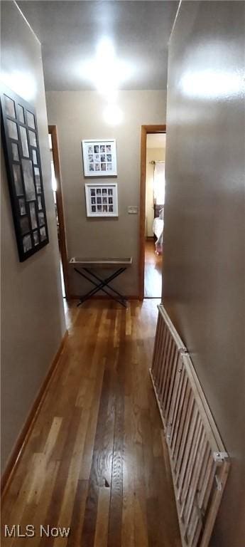 corridor featuring radiator heating unit, baseboards, and wood finished floors