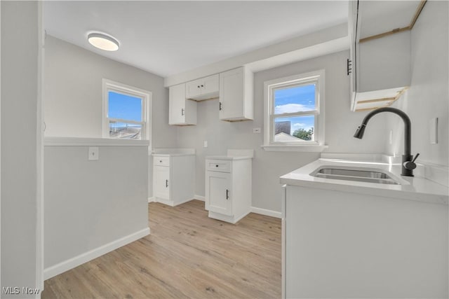 kitchen with baseboards, light countertops, light wood-style floors, white cabinets, and a sink