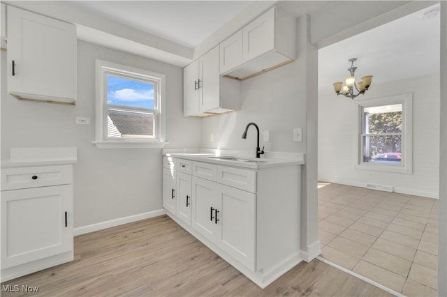 kitchen with light wood finished floors, a sink, light countertops, white cabinets, and a chandelier