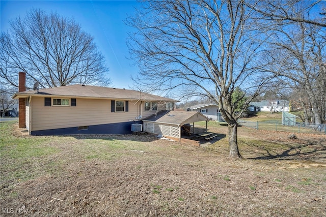 back of property featuring a carport, a lawn, a chimney, and fence