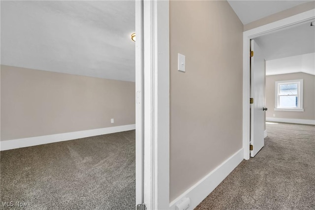 hall with baseboards, lofted ceiling, and carpet