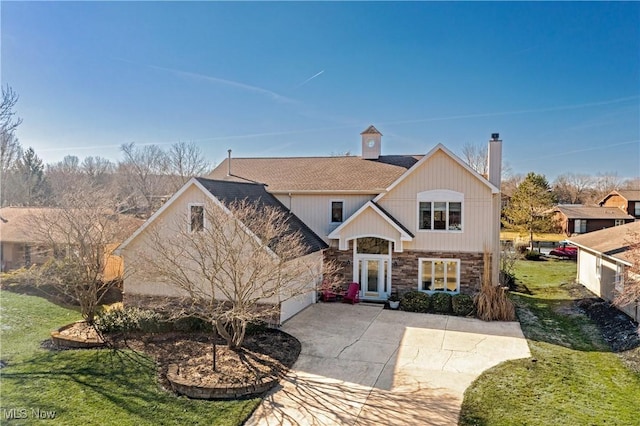 traditional-style house with stone siding, roof with shingles, a chimney, and a front yard