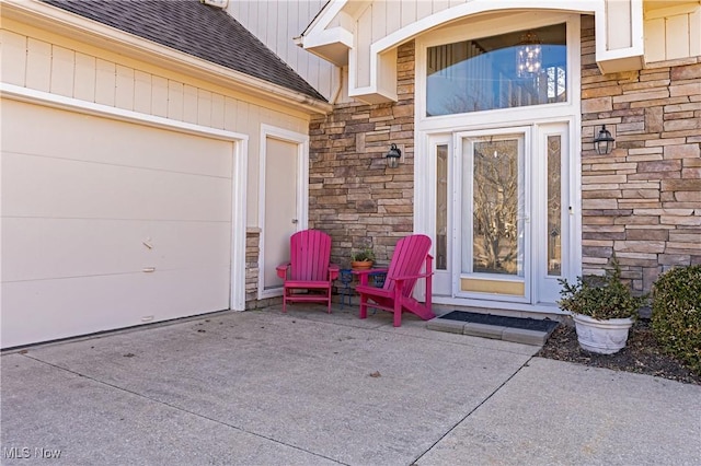 property entrance featuring stone siding, roof with shingles, and concrete driveway