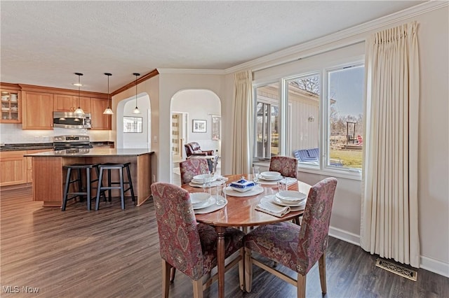 dining area featuring dark wood-type flooring, ornamental molding, a textured ceiling, arched walkways, and baseboards