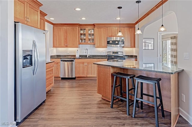 kitchen with a kitchen bar, a sink, dark wood-style floors, stainless steel appliances, and glass insert cabinets