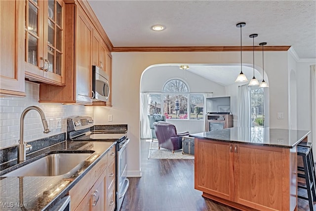 kitchen featuring dark wood finished floors, dark stone countertops, appliances with stainless steel finishes, arched walkways, and a sink