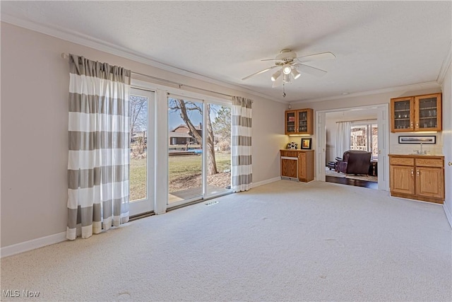 interior space featuring a textured ceiling, a ceiling fan, baseboards, and ornamental molding