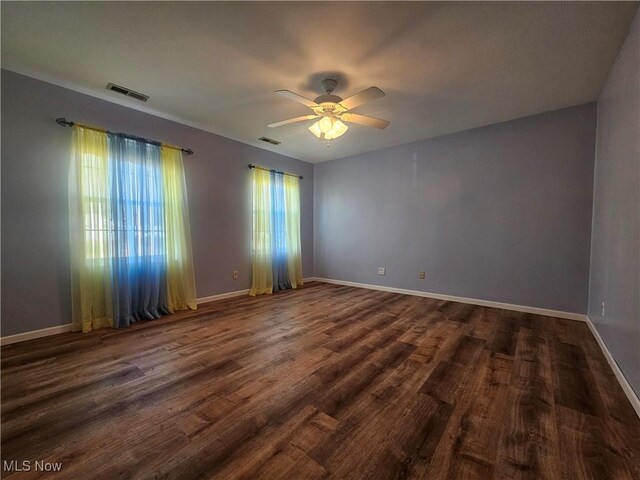 unfurnished room with baseboards, visible vents, dark wood-style flooring, and ceiling fan