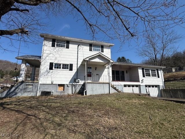 view of front of property with a porch, an attached garage, central AC unit, and a front lawn