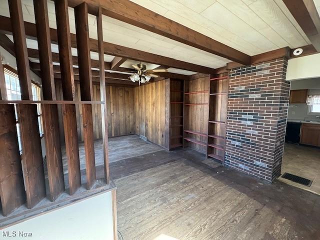 interior space featuring wooden walls, beamed ceiling, ceiling fan, and visible vents