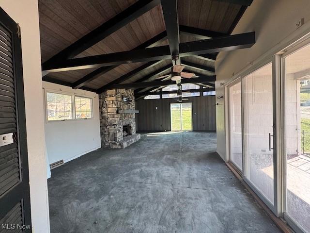 unfurnished sunroom with lofted ceiling with beams, a healthy amount of sunlight, a stone fireplace, and wooden ceiling