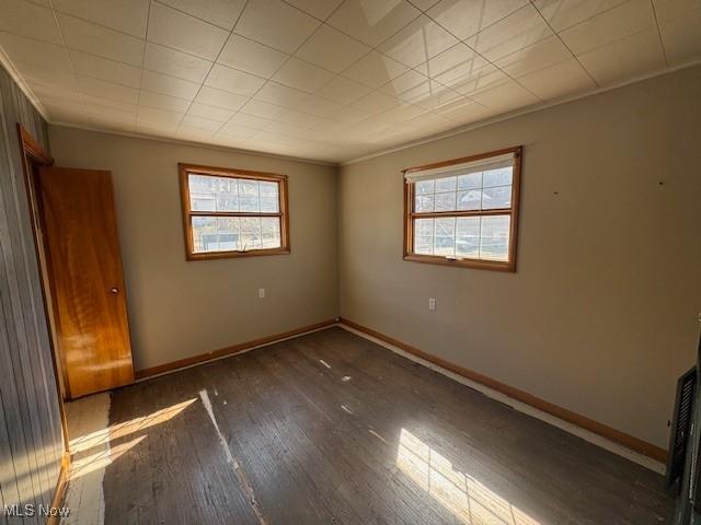 unfurnished bedroom featuring multiple windows, baseboards, wood-type flooring, and ornamental molding