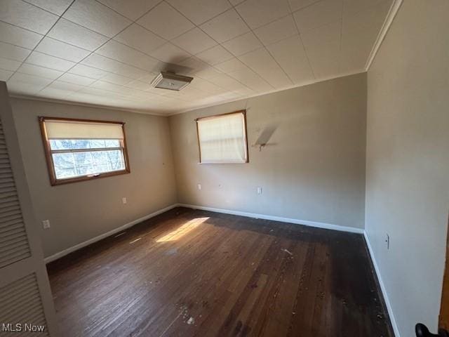 spare room featuring baseboards, wood finished floors, and crown molding