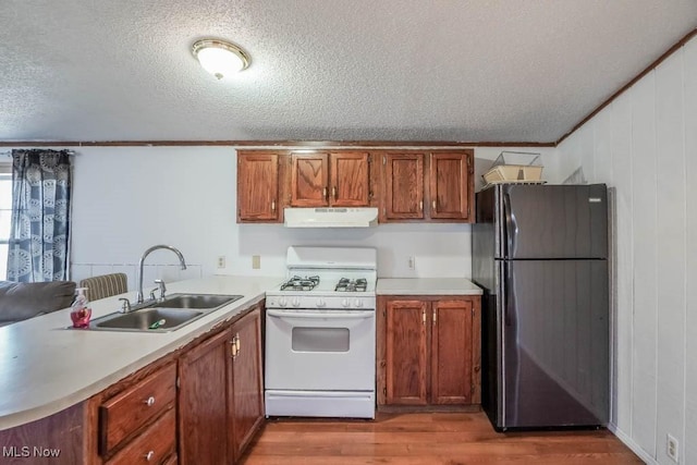 kitchen with white gas stove, under cabinet range hood, a peninsula, freestanding refrigerator, and a sink