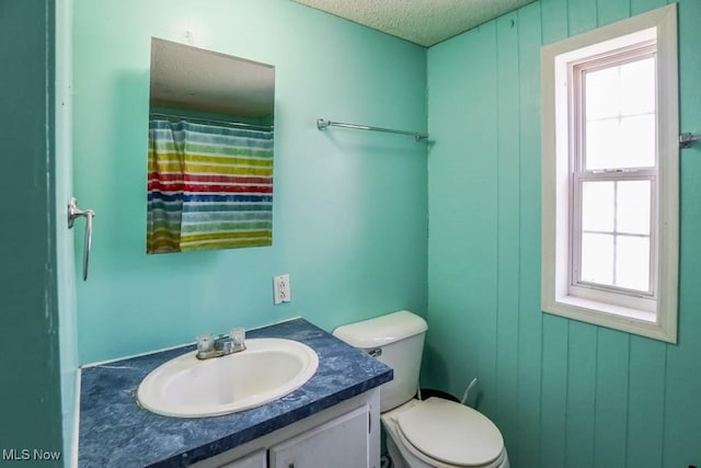 bathroom with vanity, wooden walls, toilet, and a textured ceiling