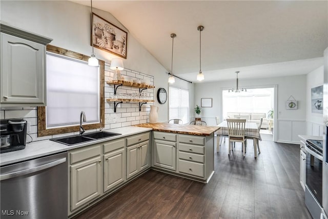 kitchen with gray cabinetry, vaulted ceiling, appliances with stainless steel finishes, a peninsula, and a sink