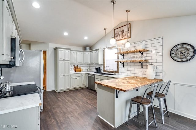 kitchen with dark wood-style floors, a peninsula, a sink, vaulted ceiling, and appliances with stainless steel finishes