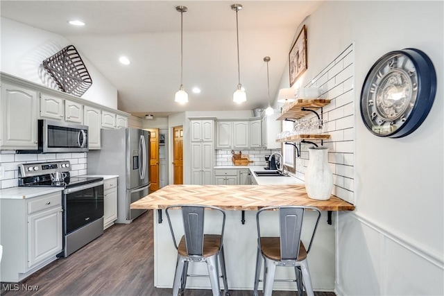 kitchen with a breakfast bar area, a peninsula, stainless steel appliances, and wood counters