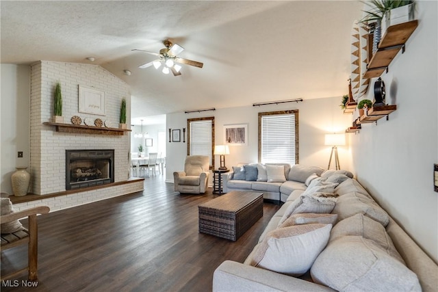 living area featuring a textured ceiling, wood finished floors, a fireplace, ceiling fan, and vaulted ceiling