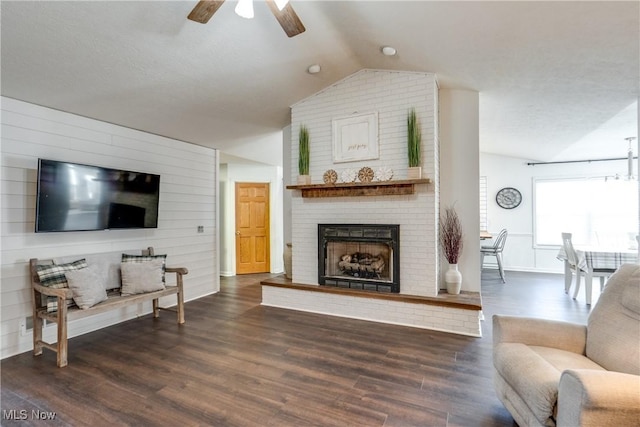 living area featuring wooden walls, dark wood-type flooring, vaulted ceiling, a fireplace, and a ceiling fan