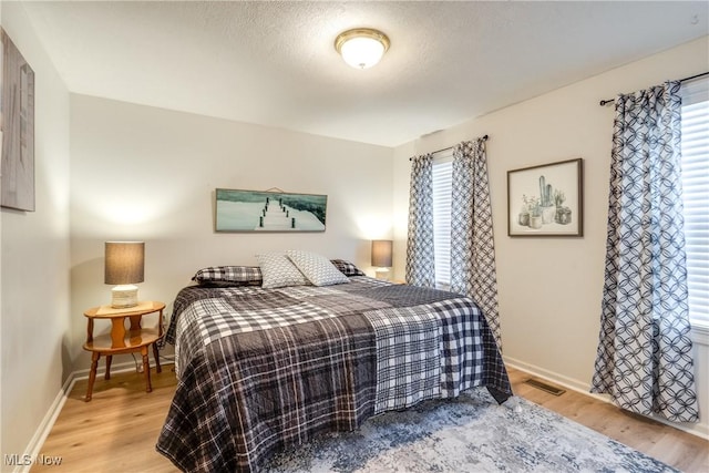 bedroom with visible vents, multiple windows, baseboards, and wood finished floors