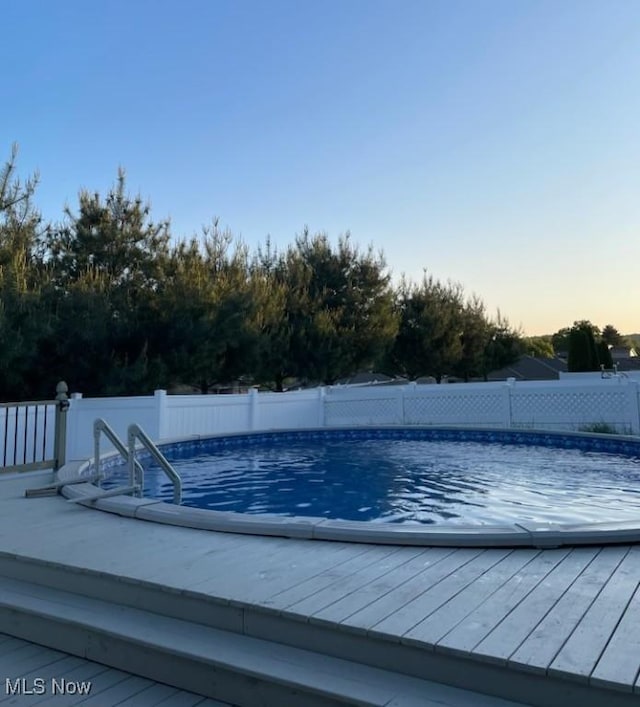 pool at dusk with a deck, a fenced backyard, and a fenced in pool