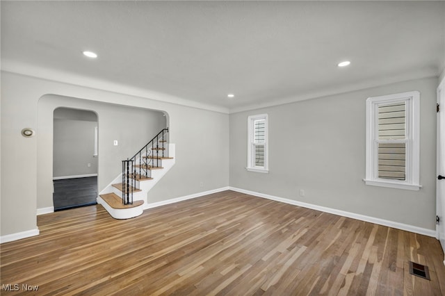 empty room with visible vents, wood finished floors, arched walkways, baseboards, and stairs