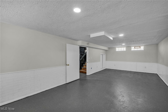 below grade area with stairway, wainscoting, and a textured ceiling