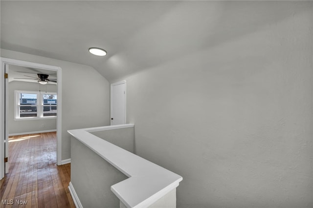 hallway with dark wood-type flooring, an upstairs landing, baseboards, and vaulted ceiling