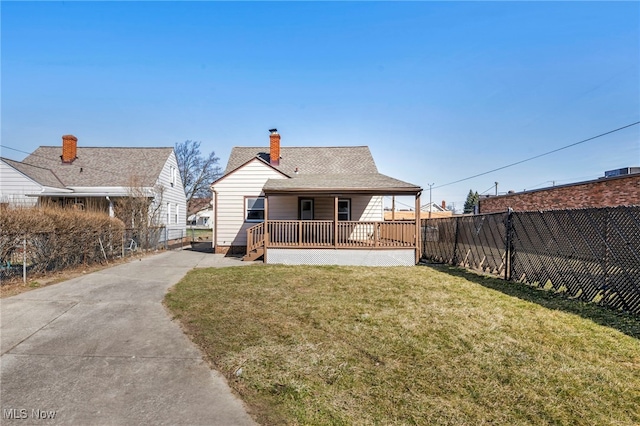 rear view of house with a porch, fence, a yard, concrete driveway, and a chimney