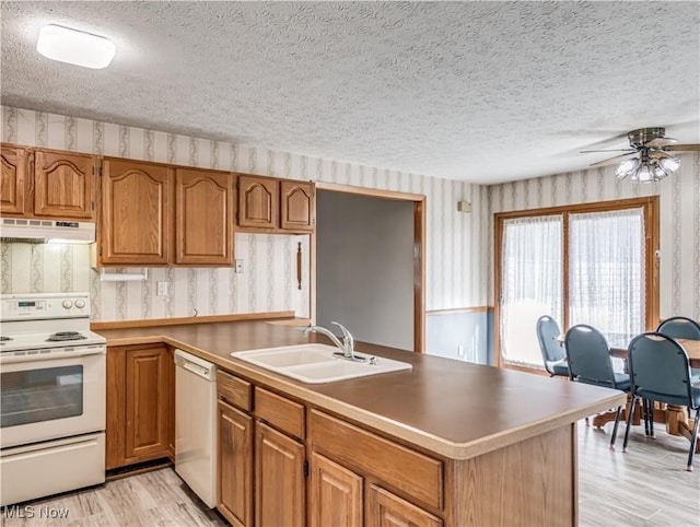 kitchen with white appliances, wallpapered walls, a peninsula, a sink, and under cabinet range hood