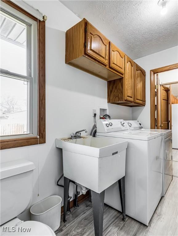 laundry room featuring washer and dryer, light wood-style floors, cabinet space, a textured ceiling, and a sink