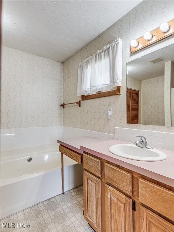 bathroom featuring vanity, a garden tub, wallpapered walls, a textured ceiling, and tile patterned floors