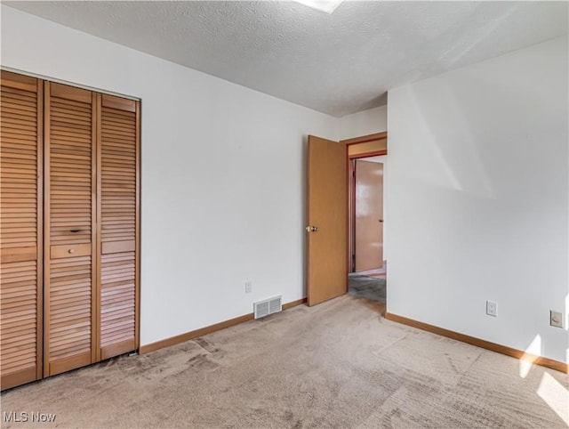 unfurnished bedroom featuring baseboards, visible vents, a closet, a textured ceiling, and carpet flooring