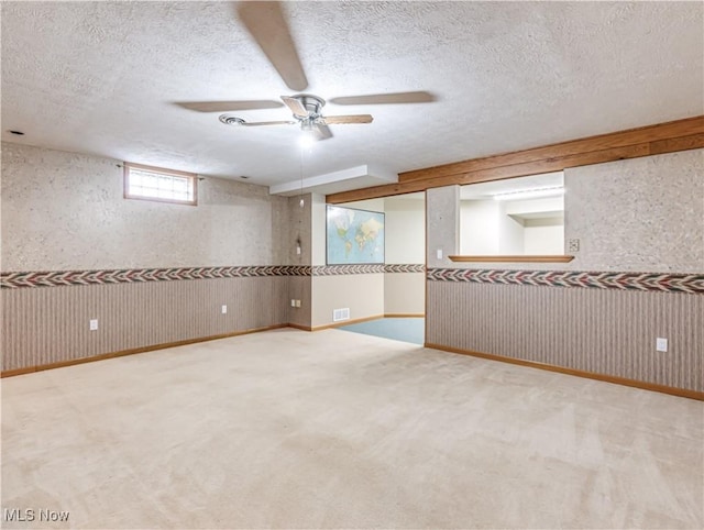 below grade area featuring visible vents, a textured ceiling, ceiling fan, and carpet flooring