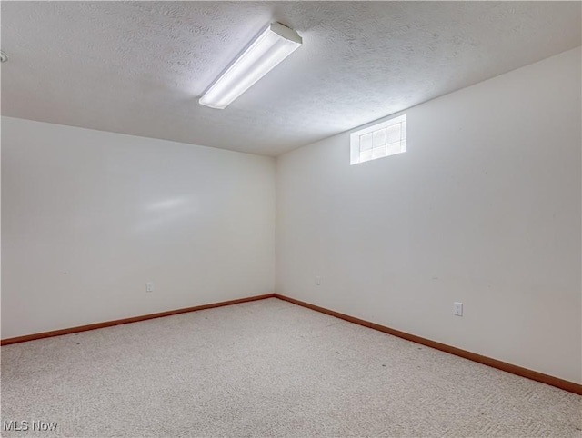 basement with light colored carpet, a textured ceiling, and baseboards