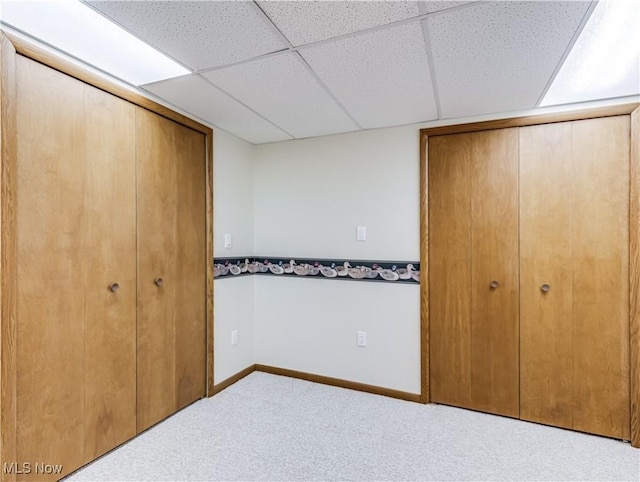 unfurnished bedroom with a drop ceiling, baseboards, and carpet flooring