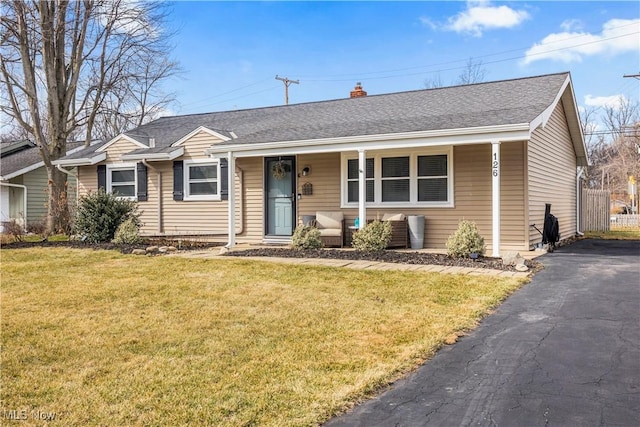 ranch-style house with a shingled roof, aphalt driveway, a front yard, covered porch, and a chimney