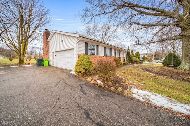 view of side of home featuring aphalt driveway, brick siding, an attached garage, and a chimney