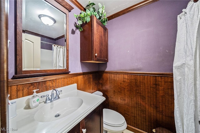 full bath featuring wood walls, toilet, ornamental molding, wainscoting, and vanity