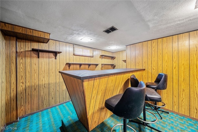 bar with visible vents, a bar, wooden walls, and a textured ceiling