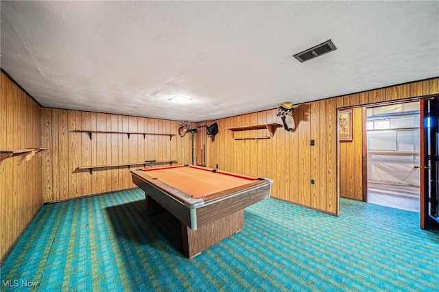 rec room featuring carpet, visible vents, wood walls, and a textured ceiling