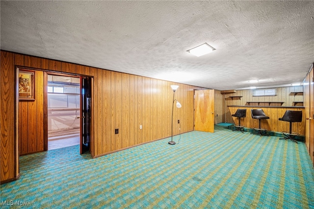 below grade area with wooden walls, a bar, carpet flooring, and a textured ceiling