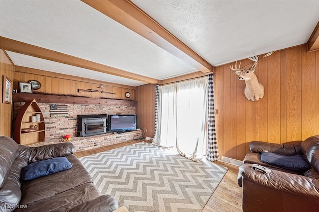 living room with wooden walls, wood finished floors, beamed ceiling, a textured ceiling, and a brick fireplace