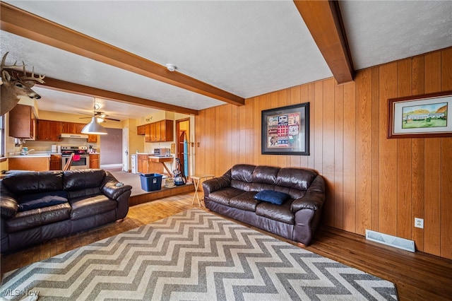 living area featuring beamed ceiling, wooden walls, wood finished floors, and visible vents