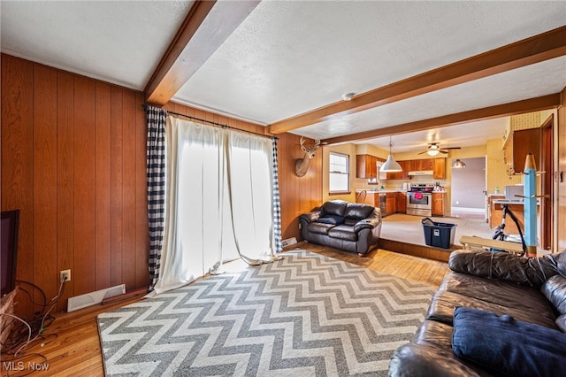 living room with visible vents, wooden walls, beam ceiling, light wood-style flooring, and a textured ceiling