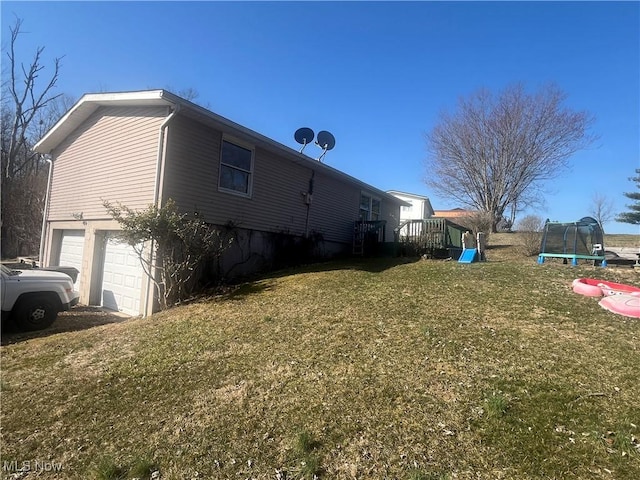 view of property exterior with a trampoline, a lawn, and an attached garage