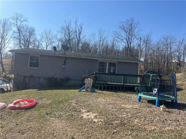 rear view of house featuring a yard, a trampoline, and a wooden deck