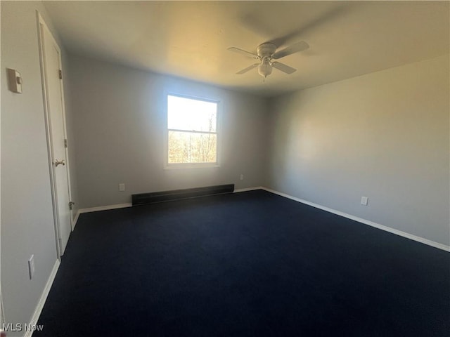 empty room with dark carpet, baseboards, ceiling fan, and a baseboard radiator