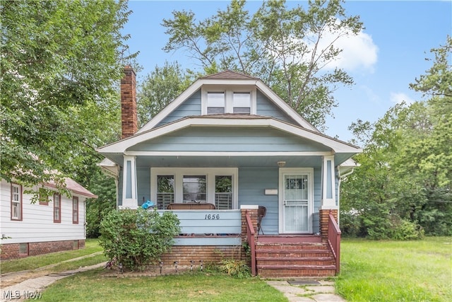 bungalow-style house with a chimney, covered porch, and a front yard